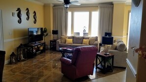 A living room with a television, two sofas, a red armchair, and decorative seahorse wall art.