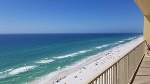 A beach view from a balcony with a railing, ocean waves, and beachgoers.