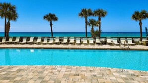 A poolside area with lounge chairs and palm trees, overlooking a clear blue ocean.