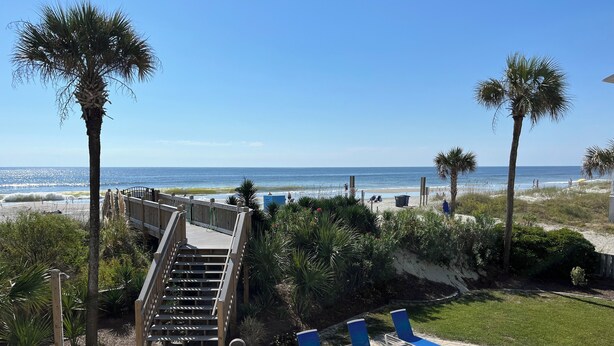 Une vue sur la plage avec un escalier en bois menant à une terrasse, des chaises longues et des palmiers.