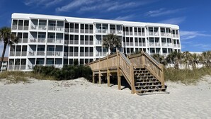 Un hôtel à plusieurs étages, doté de balcons et d’un escalier en bois menant à la plage.