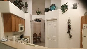 A kitchen with wooden cabinets, a microwave, a stove, and a sink. There is a door leading to another room. - Elegant Paradise Villa...Disney Luxury Vacation Home (Clermont)