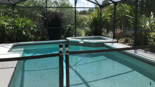 A covered outdoor swimming pool with a safety fence, surrounded by lush greenery and a clear sky. - Elegant Paradise Villa...Disney Luxury Vacation Home (Clermont)