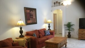 A living room with a red sofa, two side tables with lamps, a wooden coffee table, and a television on a wooden cabinet. - Elegant Paradise Villa...Disney Luxury Vacation Home (Clermont)