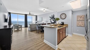 A modern kitchen with a central island, a dining area with a sofa and chairs, and a large window offering a view.