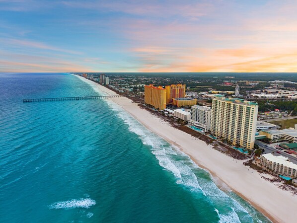 Un hotel costero con varios edificios altos, una playa y un muelle que se adentra en el océano.