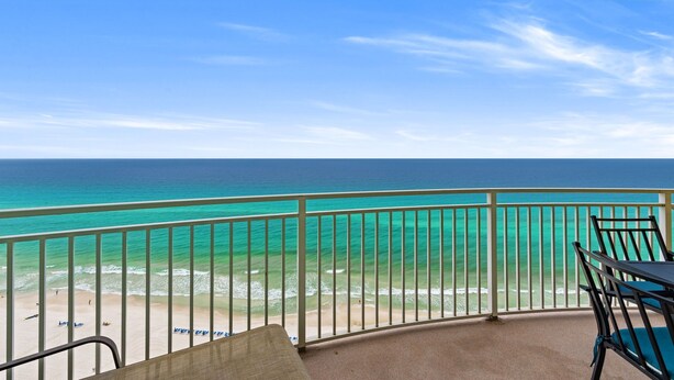 A balcony with a view of the ocean, a table, and chairs.
