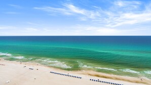 A beach with clear blue water, a sandy shore, and a row of blue lounge chairs.