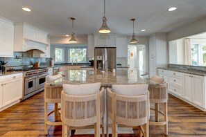 Una cocina amplia con una isla central, armarios blancos y un refrigerador de acero inoxidable.