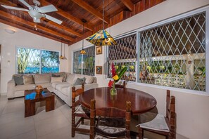 A spacious living area with a wooden ceiling, a round wooden dining table, and a large window with a view of the outdoors.