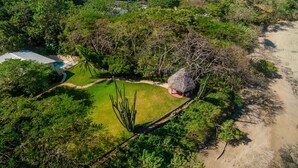 An aerial view of a property with a thatched-roof hut, a swimming pool, and lush greenery. - Tamarindo's Hidden Gem, Tropical oasis 3 BR Beachfront Home, with private pool.
 (Tamarindo)