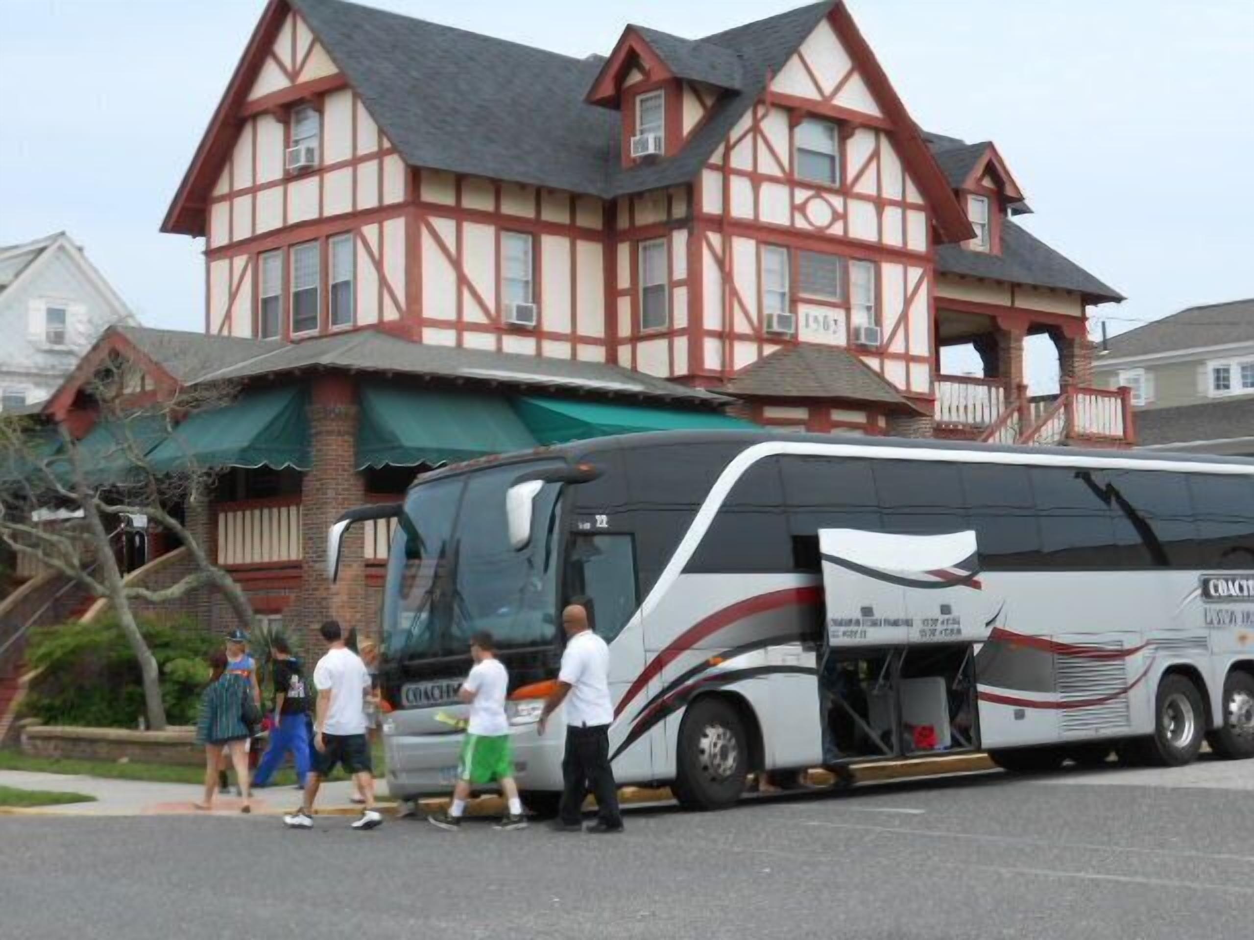 Un autocar est garé devant un bâtiment de style Tudor, avec une façade en briques et un auvent vert.