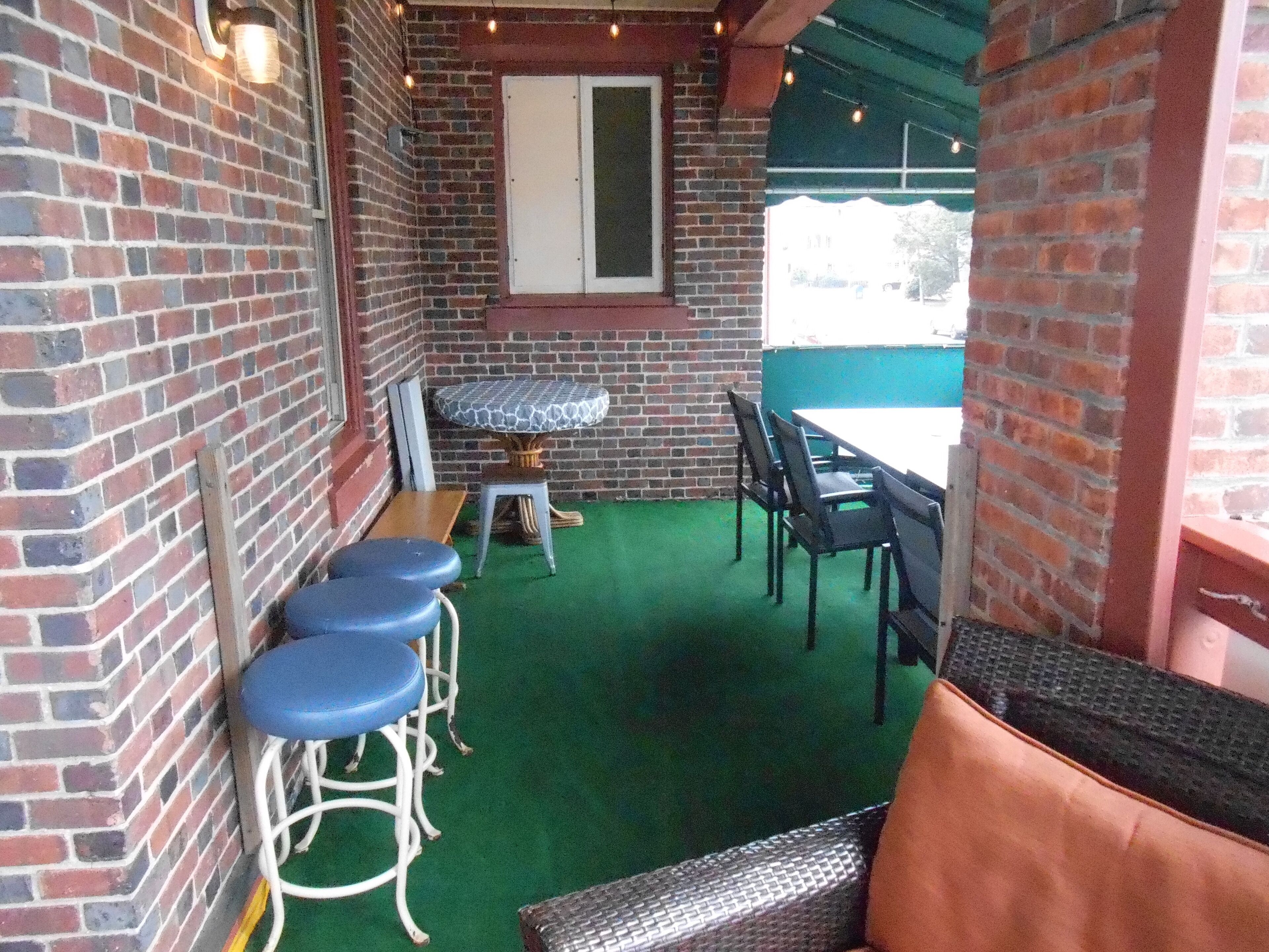 A covered patio area with brick walls, a green artificial turf floor, and outdoor furniture including a table and chairs.