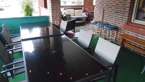 Ein Außenbereich mit einer langen schwarzen Tischplatte, weißen Stühlen, einer Couch und einem Barhocker.