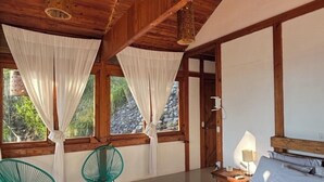 Un dormitorio tipo cabaña de madera con una cama, dos sillones, una mesita de noche y una ventana con cortinas.