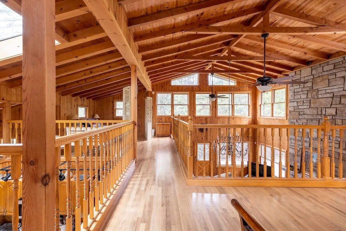 Un intérieur spacieux en bois, avec un plafond haut, un mur en pierre et un escalier central.