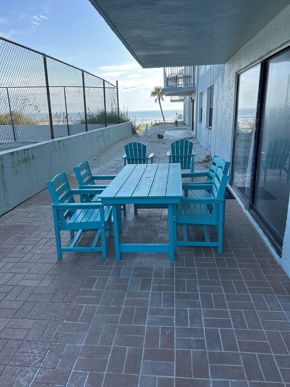 A patio with a table and chairs, a fence, and a view of the beach.