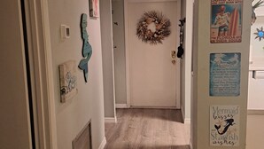 Un couloir doté d’un plancher en bois, une porte ornée d’une guirlande et divers éléments de décoration murale, notamment des panneaux et une affiche.