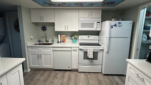 Une cuisine avec des meubles blancs, un four à micro-ondes, une cuisinière et un réfrigérateur.