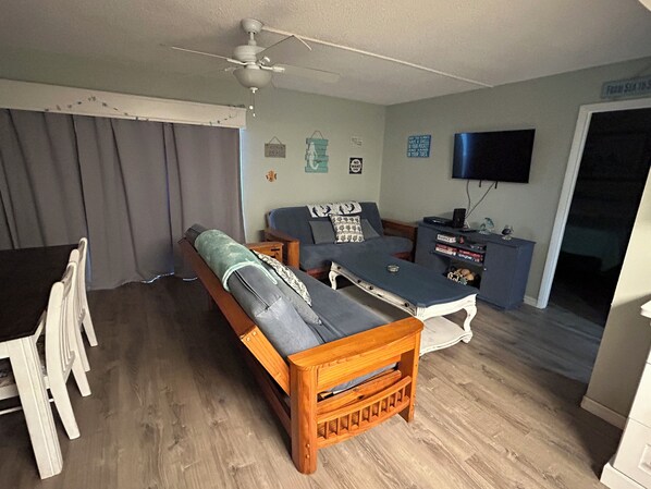 A living room with a sofa, a wooden bench, a TV, and a small table. - Easy access ground floor unit close to parking lot, conveniently located to all NSB has to offer (New Smyrna Beach)