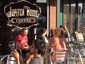 Relax in the casual outdoor seating area of Jupiter House Coffee, where metal chairs and tables invite conversation and a moment to unwind.