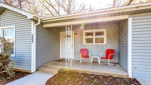 A house with a covered porch, two red chairs, and a small garden with flowers. - Charming Stones Throw Cottage walk to UNT! (Denton)