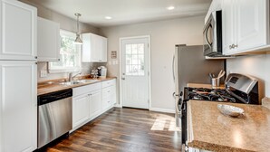 A modern kitchen with white cabinetry, a stainless steel dishwasher, a built-in oven, and a microwave. - Charming Stones Throw Cottage walk to UNT! (Denton)