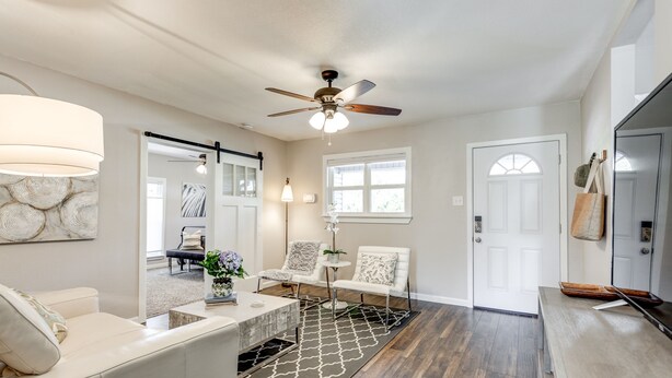 A modern living room with a ceiling fan, a white sofa, a coffee table, and a patterned rug. - Charming Stones Throw Cottage walk to UNT! (Denton)