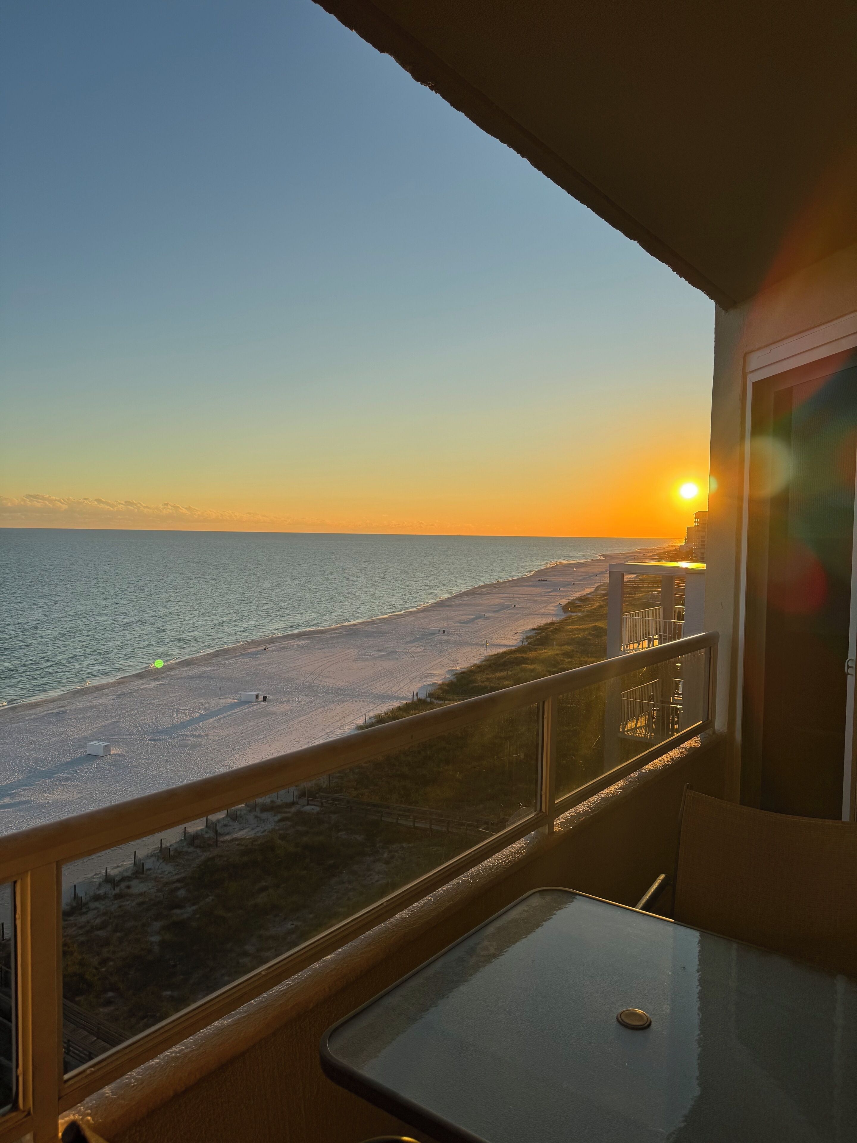 A balcony with a view of the beach and ocean during sunset.