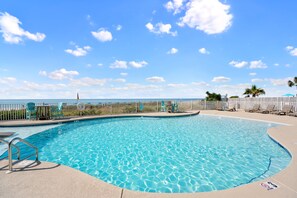 A clear blue swimming pool with a wooden deck, lounge chairs, and a view of the ocean.