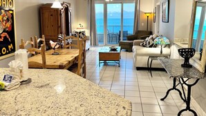 Ett rymligt vardagsrum med en köksö, matbord och sittgrupper. Ett stort fönster ger utsikt över havet.