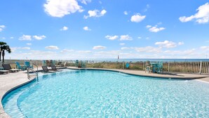 En vacker, klarblå pool med en träbrygga, solstolar och utsikt över havet.
