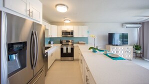 A modern kitchen with stainless steel appliances, a central island, and a flat-screen TV.