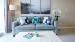 A living room with a light blue sofa, a white coffee table, and a framed seascape painting above the sofa.