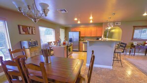 A spacious kitchen with wooden cabinets, a central island, and a dining area with wooden chairs. - A Desert Bloom House (Page)