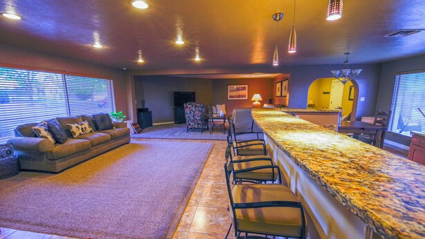 A spacious living area with a large sofa, a dining table with bar stools, and a kitchen in the background. - A Desert Bloom House (Page)