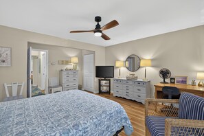 Une chambre à coucher comprenant un lit, un bureau, une chaise, un téléviseur et un ventilateur de plafond.