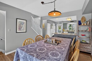 Un coin repas avec une nappe à motifs, des chaises en bois, un luminaire suspendu et un escalier menant à une autre pièce.