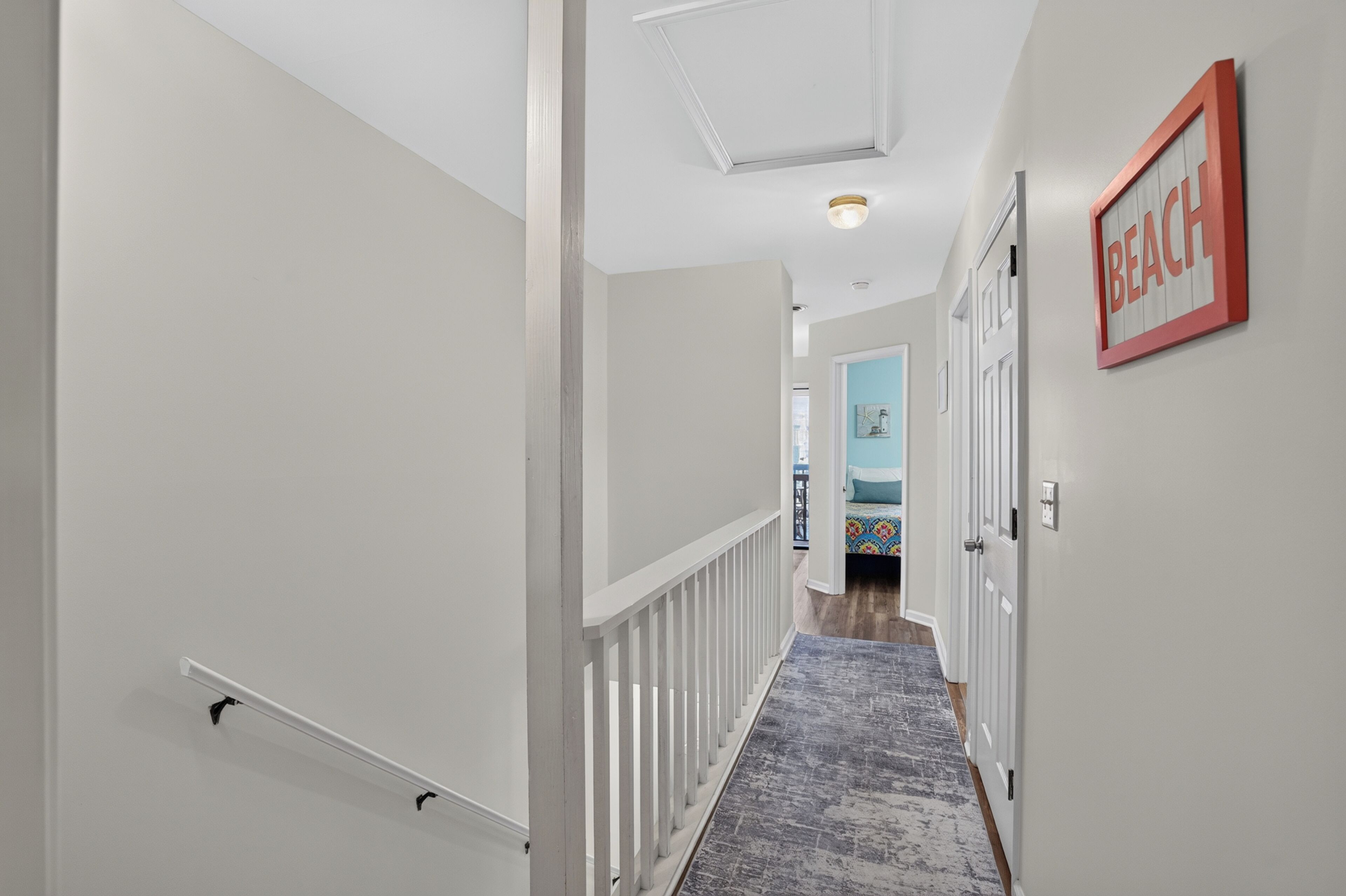 A hallway with a white railing, a patterned rug, and a door with a 'BEACH' sign.
