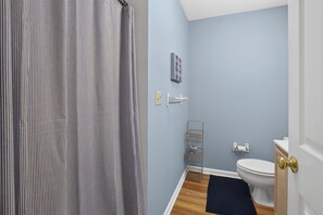 Une salle de bain avec un rideau de douche, des toilettes, un lavabo, un porte-serviettes et une petite étagère.