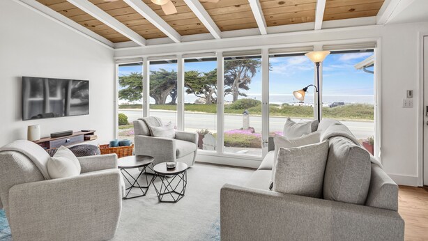 Un salon spacieux doté d’un ventilateur de plafond, de grandes fenêtres et d’une vue sur la plage.