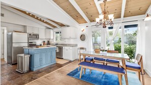 Une cuisine moderne avec des meubles blancs, un îlot central bleu, des appareils en acier inoxydable et un coin repas comprenant une table en verre et des chaises bleues recouvertes de tissu.