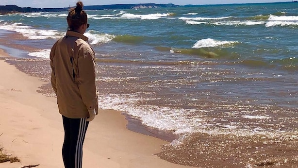 En person står på en sandstrand och blickar ut mot havet.