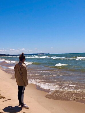 A person standing on a sandy beach facing the ocean.