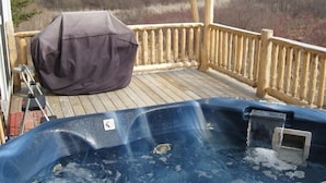 Ett trädäck med ett bubbelbad, en möblerad uteplats och utsikt över ett vackert naturlandskap.