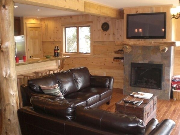 A cozy living room with a leather sofa, a fireplace, and a television mounted on the wall.