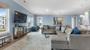 A spacious living room with a large sectional sofa, a flat-screen TV, and a dining area with a kitchen counter. - ☀️ The Beach House | Designer 7BR w/ Huge Pool, Bunk Room + In-Law Suite (Pensacola Beach)