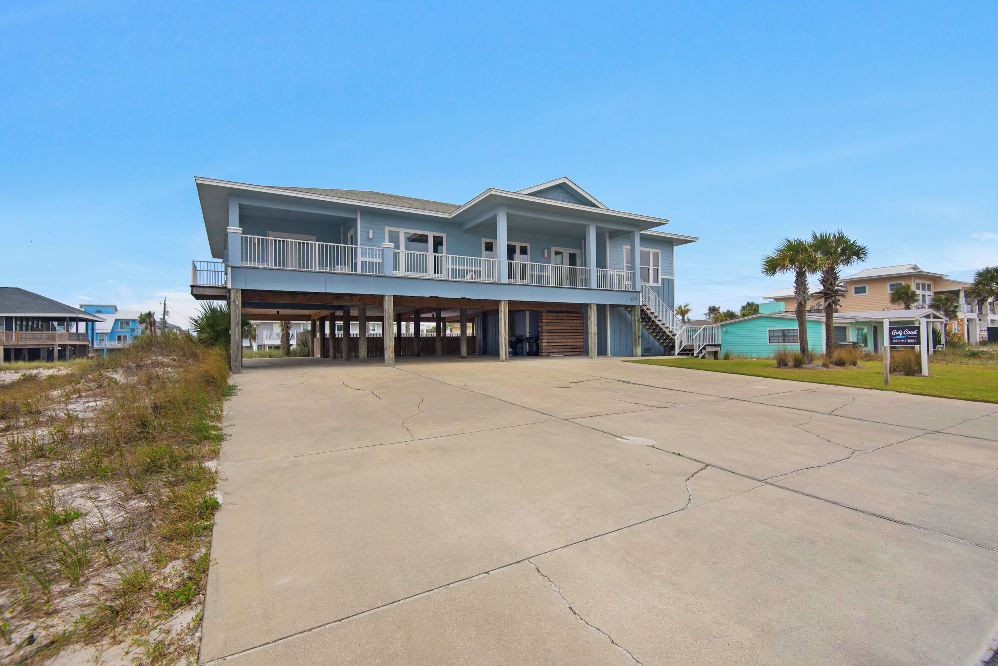 A two-story beachfront house with a balcony, a covered garage, and a clear view of the beach.