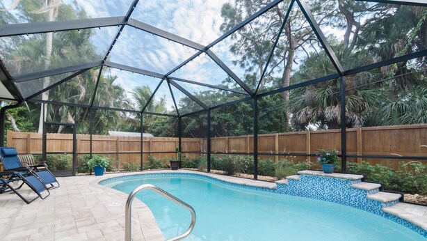 Un espace piscine doté d’une enceinte en verre, de chaises longues et d’une clôture en bois.