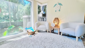 A room with a large window, two chairs, a small table with a lamp, and a decorative turtle wall piece.